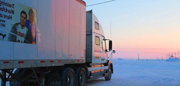 A semi truck in a snowy area with the sun setting.